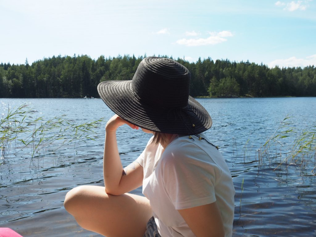 Hattupäinen nainen katsoo järvelle aurinkoisena päivänä.