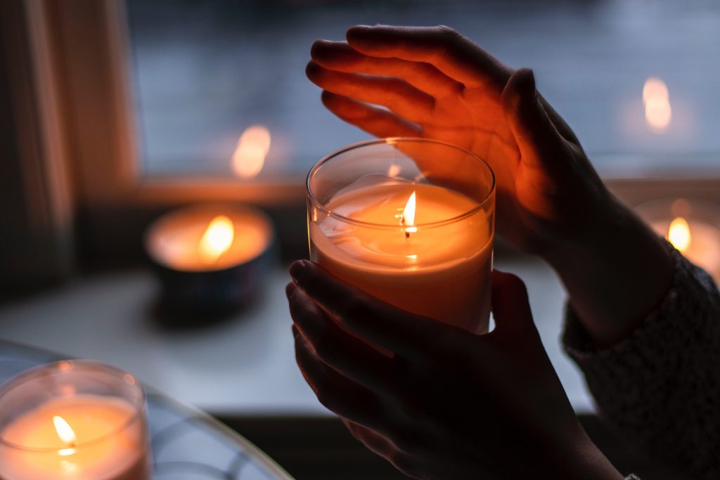 Henkilö pitää toisessa kädessään palamassa olevaa kynttilää ja suojaa toisella kädellä kynttilän liekkiä.